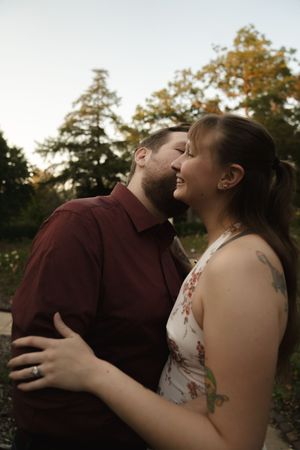 A romantic couple shares an intimate moment outdoors during golden hour with autumn trees in the background.
