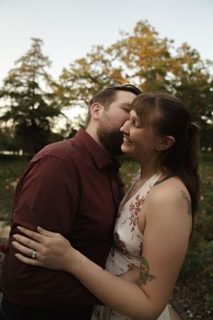 A tender moment between a couple in a burgundy shirt and floral dress against a fall backdrop.
