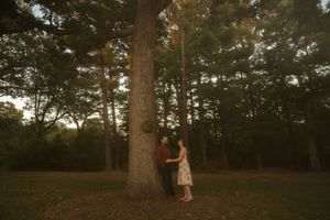 A romantic evening photoshoot of a couple by a majestic tree in a wooded area.