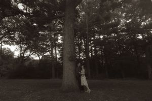 A vintage-style black and white photo of a couple embracing by a large tree.
