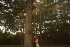 A couple shares a romantic moment against a tall tree trunk during sunset in a forest.