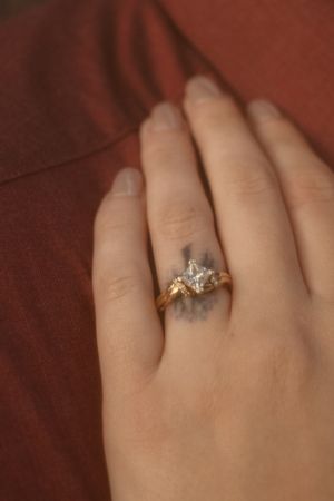 Close-up of an engagement ring with unique design worn on a hand against burgundy fabric.