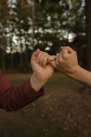 Two hands making a pinky promise gesture outdoors in natural lighting.
