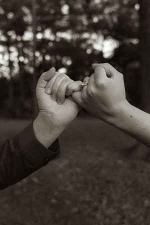 Black and white image of two hands making a pinky promise against a blurred forest background.