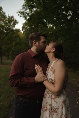 A couple shares a romantic kiss in a park setting during golden hour.