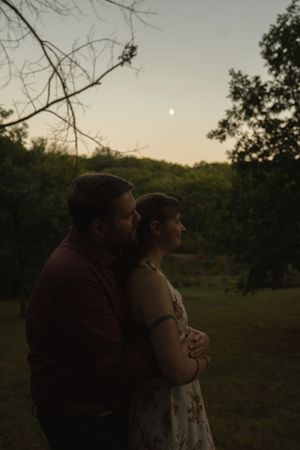 Couple embracing in a field at sunset with trees in background.