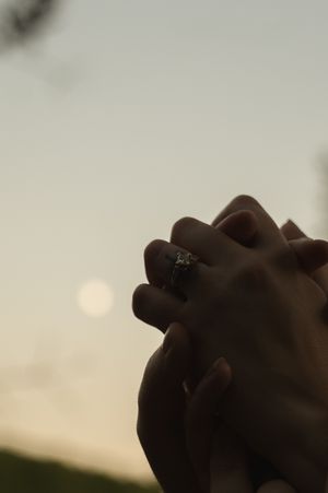 Close-up of hands with engagement ring against sunset sky.