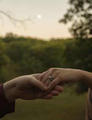Two hands reaching towards each other with engagement ring visible at sunset.