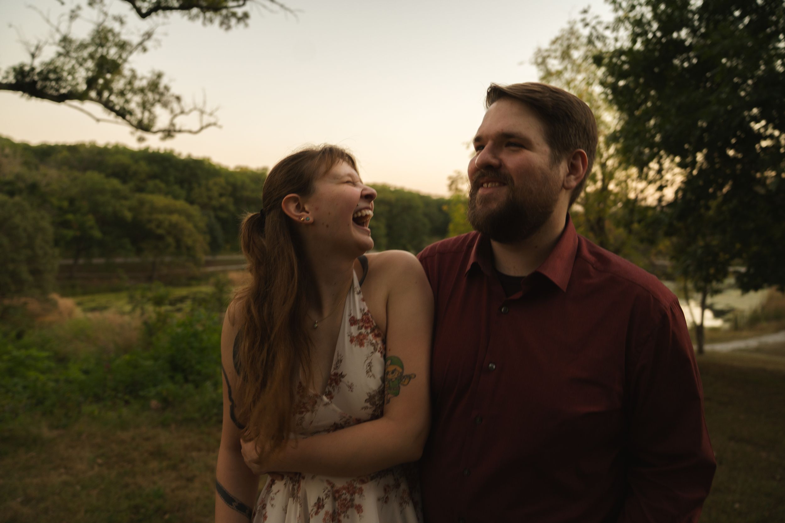 Intimate couple embracing at sunset with trees and nature in background.