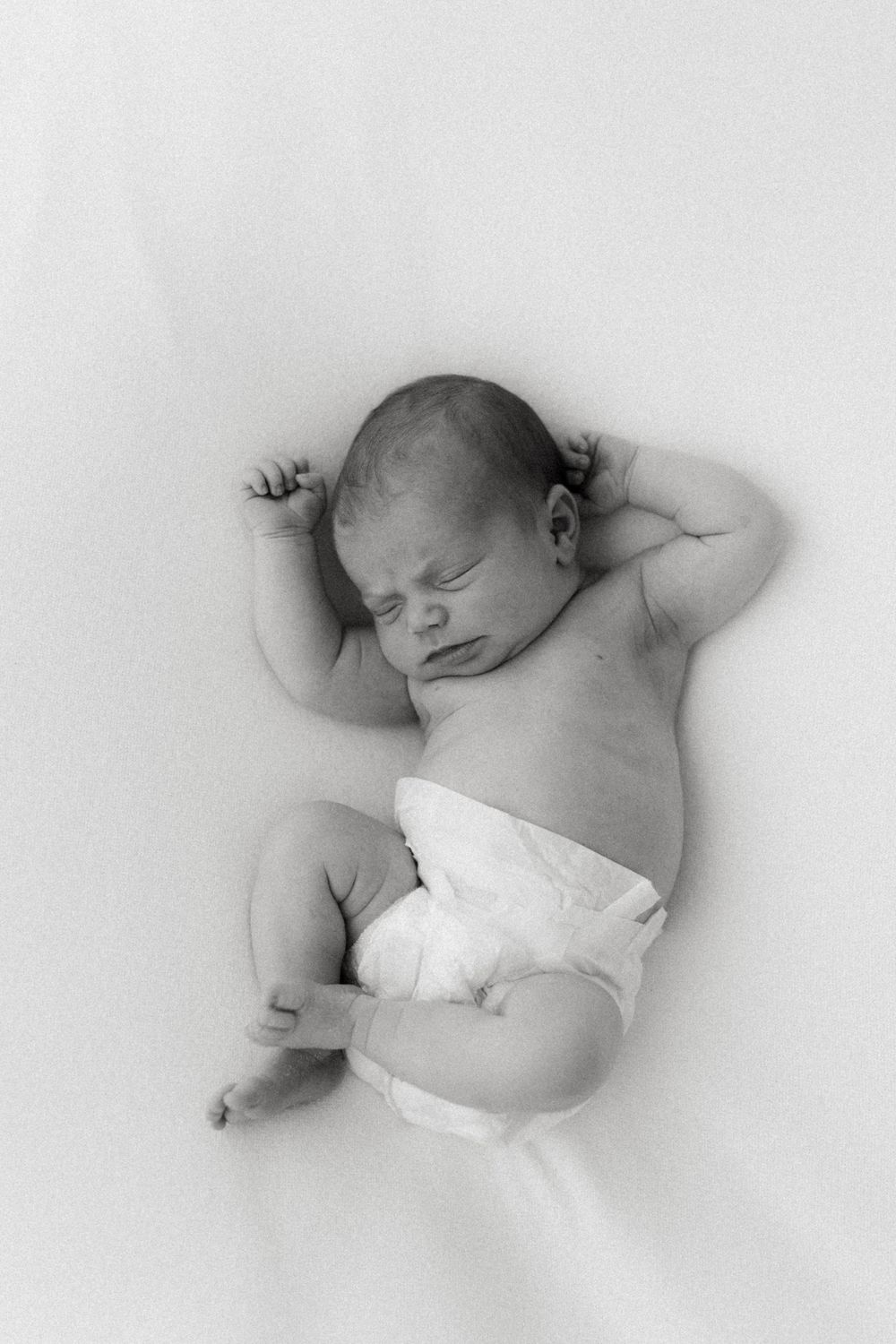 A series of black and white photographs showing a sleeping newborn baby in various peaceful resting positions.