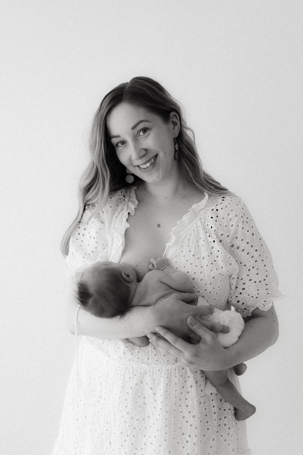 A tender black and white portrait series showing nurturing moments between parent and infant in matching white attire.