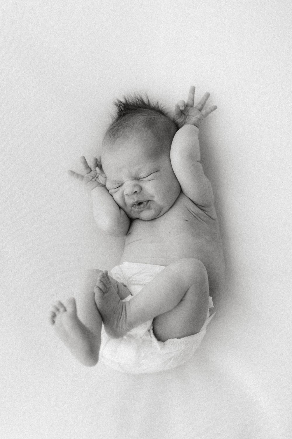 A series of black and white photos showing a sleeping newborn baby in white diaper on white background.