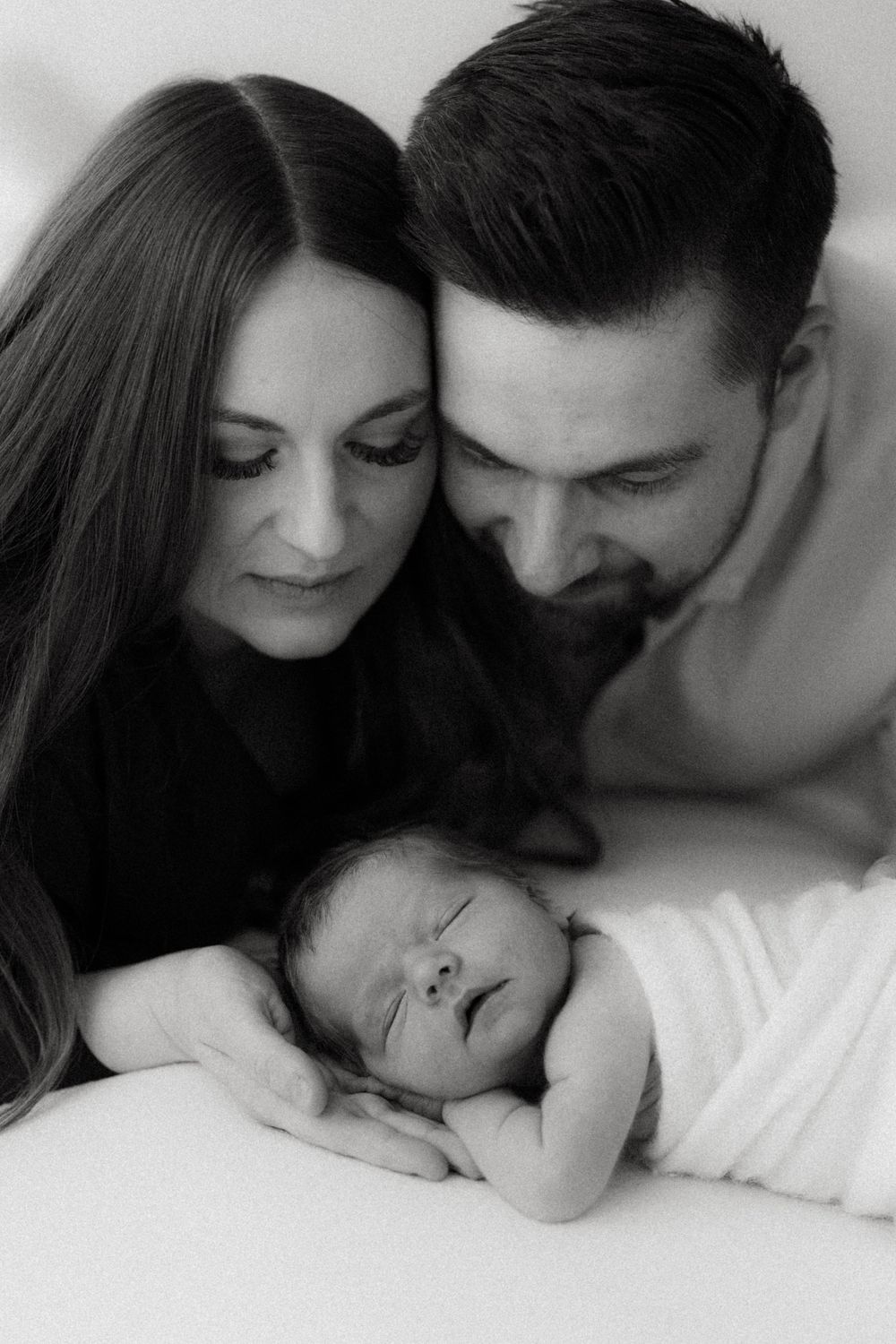 Black and white photo series showing intimate family moments with parents and newborn baby in tender poses.