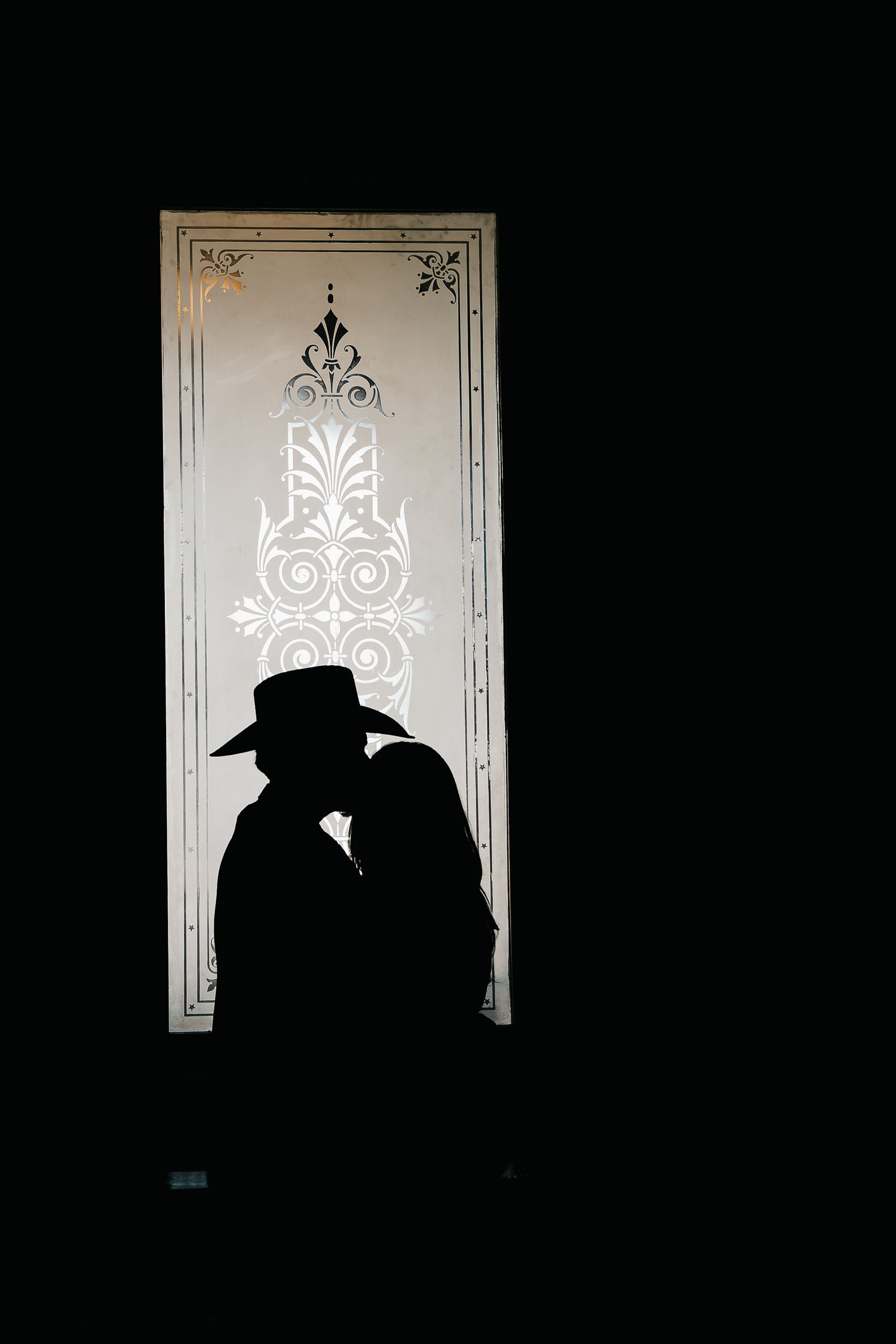 A romantic couple poses on an elegant dark staircase in contrasting white and gray outfits for their engagement photos.