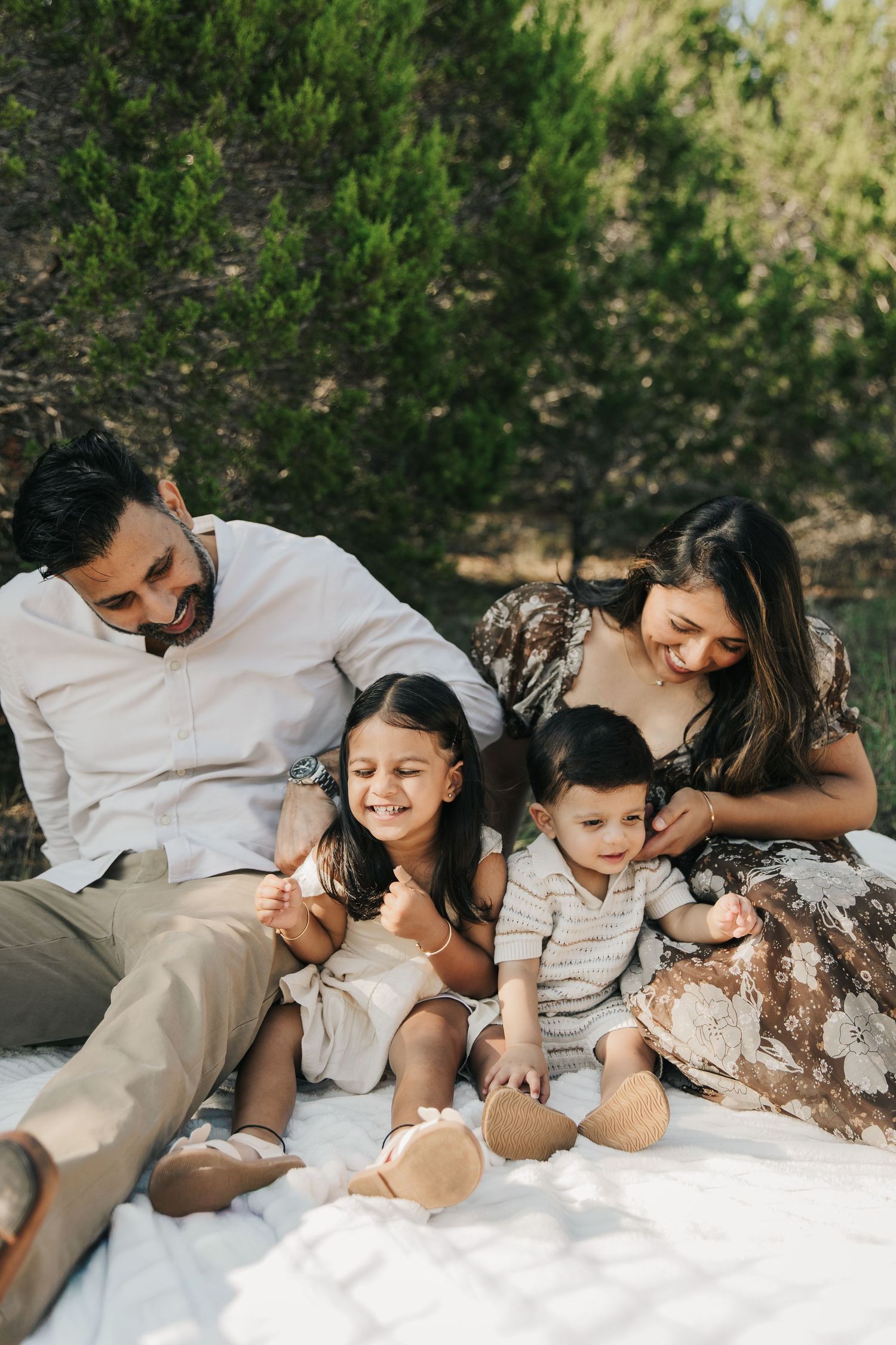 A family shares tender moments together while relaxing on a white blanket outdoors in nature.