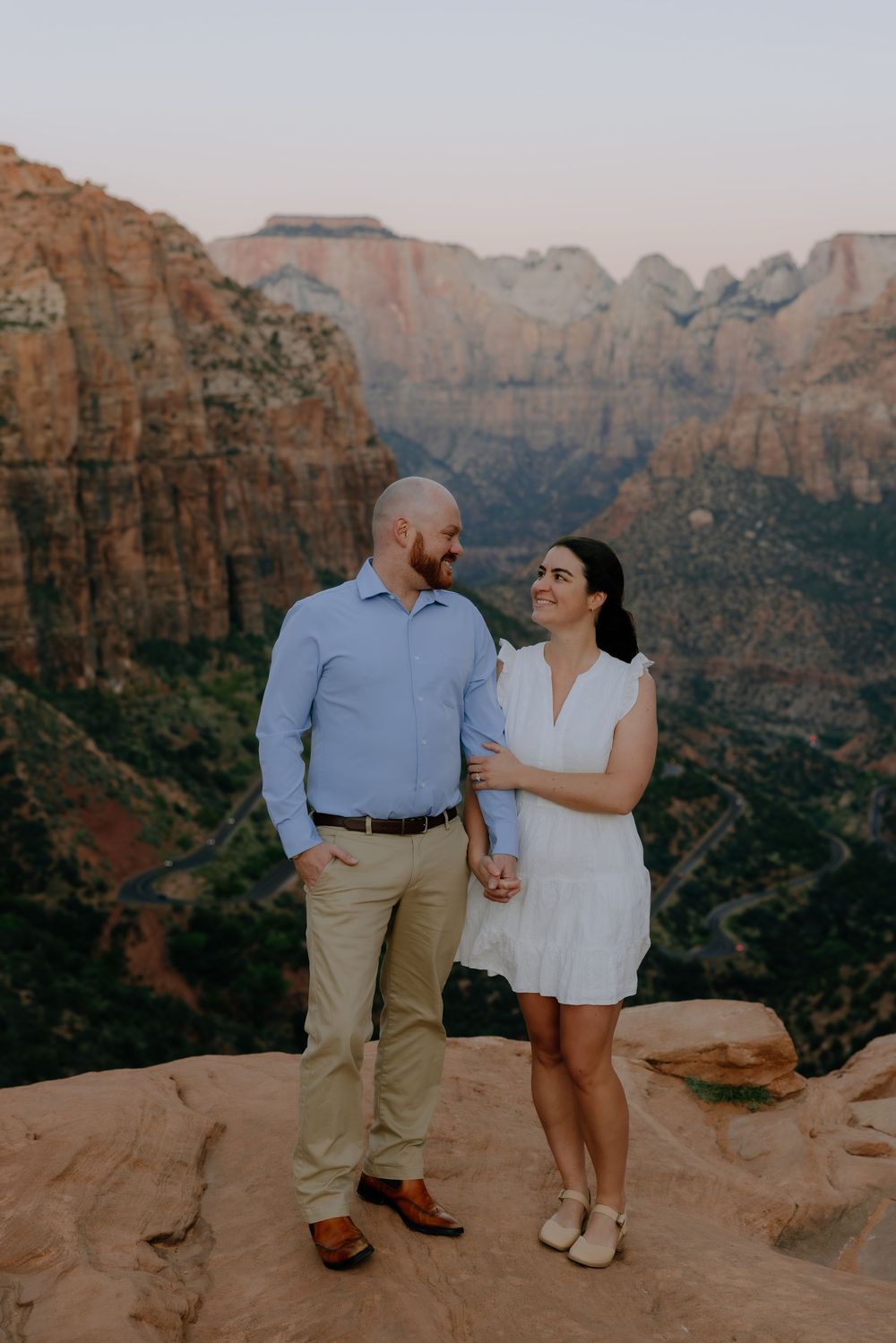 A couple shares a romantic moment on red rocks overlooking majestic canyon cliffs at sunset.