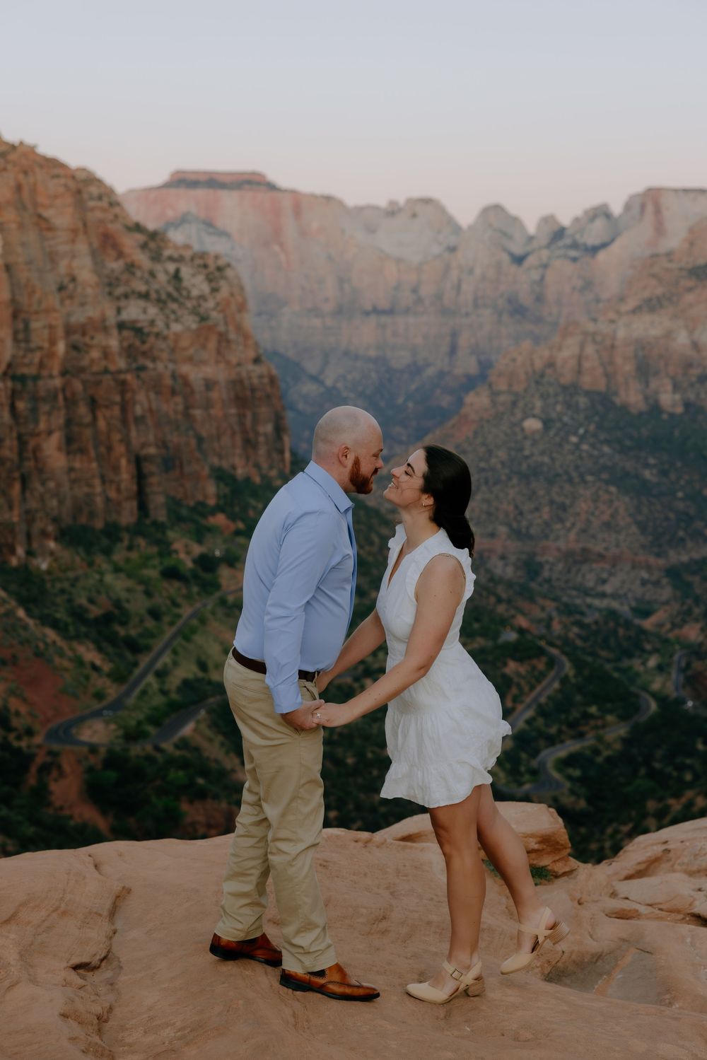Romantic couple embraces on red rock cliff edge with dramatic canyon landscape at sunset.