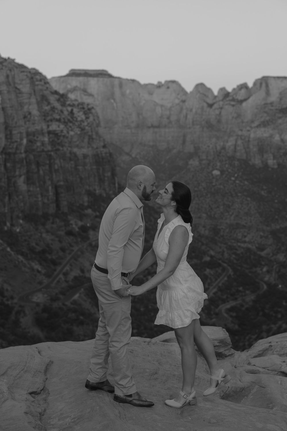 A black and white photograph captures an intimate moment between a couple against majestic canyon landscapes.