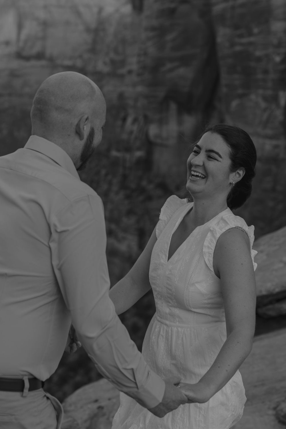 A joyful black and white moment captured between two people against a rocky canyon backdrop.