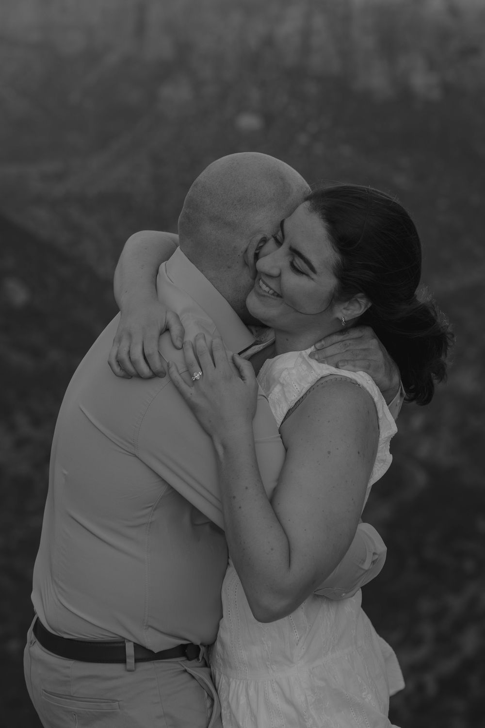 Black and white photo of intimate embrace against dramatic mountain backdrop at dusk.