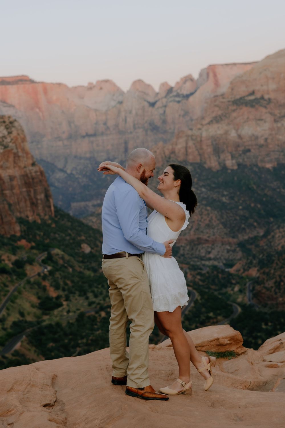 A couple dances together on red rock cliffs overlooking a scenic canyon vista at sunset.