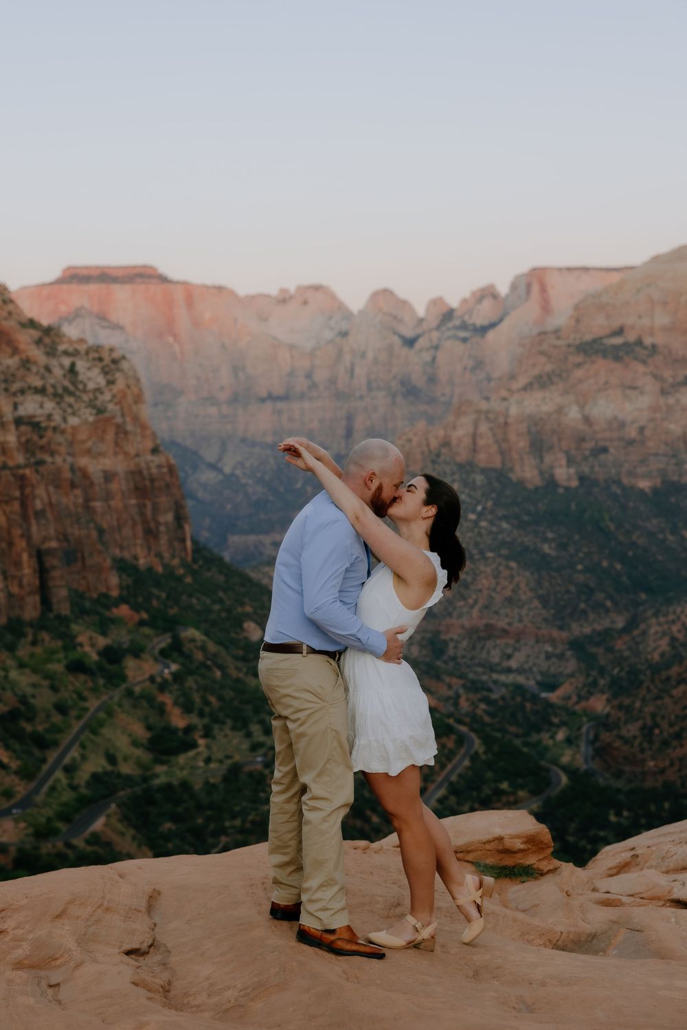 A romantic couple embraces while standing on desert cliffs with dramatic canyon views in the background.
