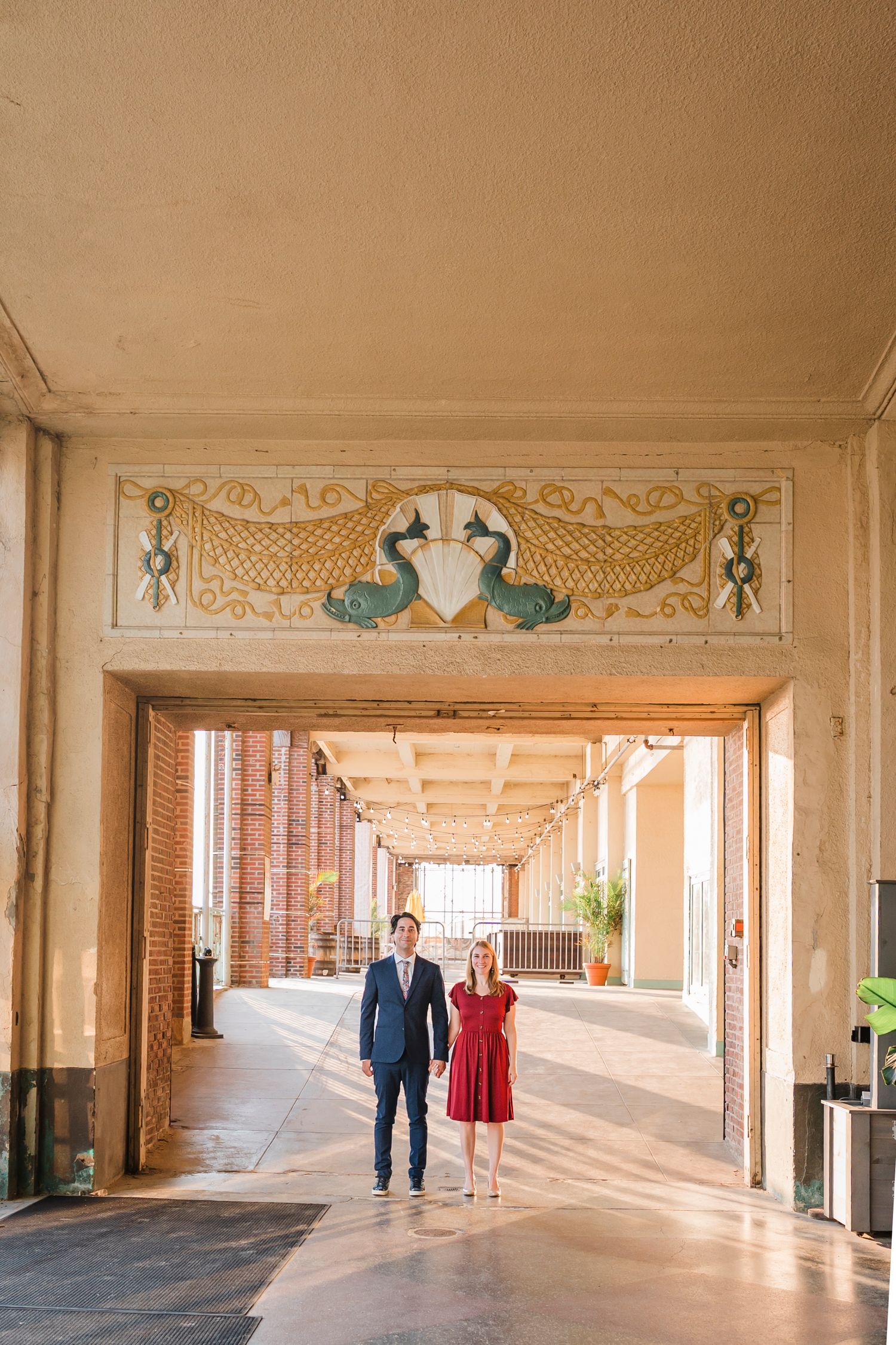 Couple walking through an elegant colonnade hallway with ornate architectural details and natural lighting.