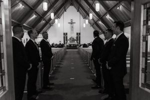 Wide panoramic view of wedding guests standing in church pews during ceremony.