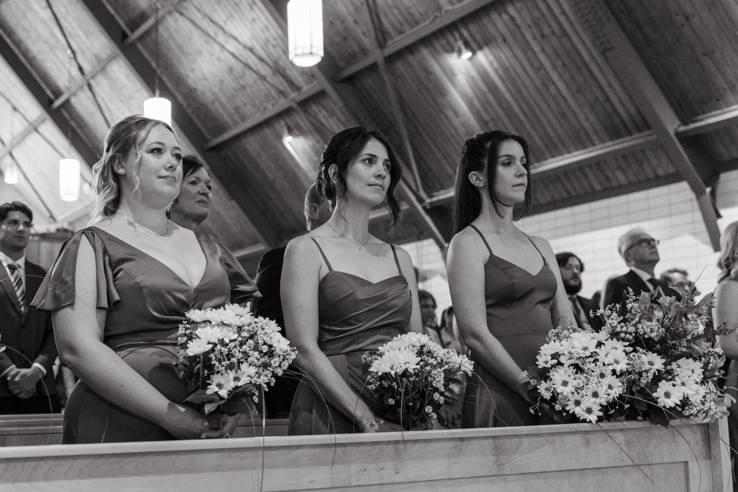 Row of bridesmaids in formal dresses holding bouquets during church wedding ceremony.