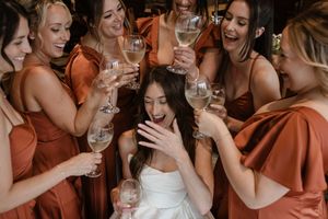 Wedding party in orange bridesmaid dresses laughing and celebrating with champagne glasses at a reception.