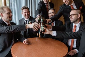 A group of people in business attire toasting with beer bottles around a wooden table.