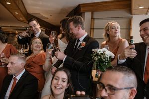 Wedding guests laugh and celebrate during a joyous reception gathering indoors.
