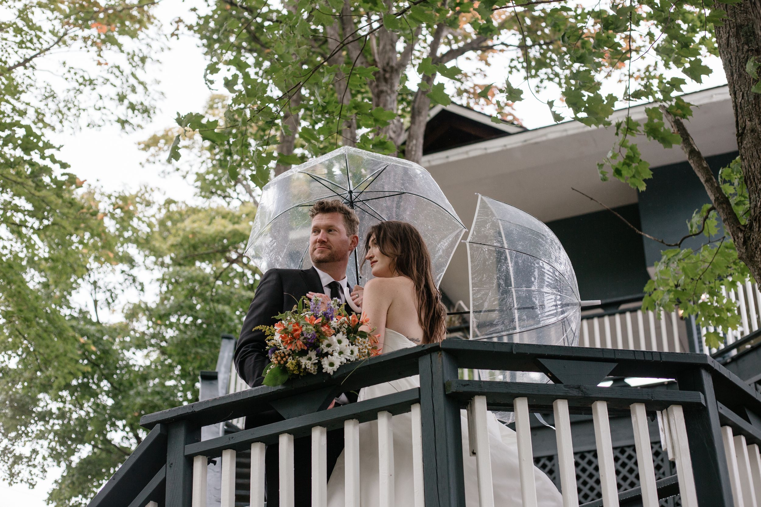 A romantic outdoor wedding moment captured on a wooden deck surrounded by lush green trees.