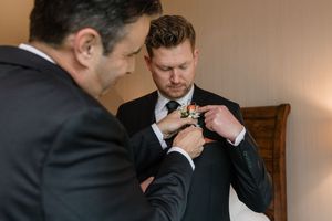 Groom adjusts his tie while getting ready for wedding ceremony in elegant indoor setting.