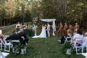 Wedding ceremony setup in an outdoor wooded area with white chairs and floral decorations.