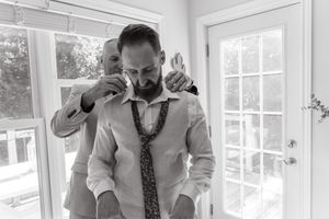 Black and white photo of someone adjusting a patterned necktie while standing in front of bright windows.