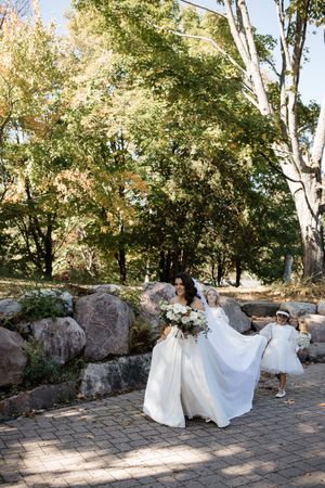 A bride in a flowing white wedding dress twirls gracefully on a stone patio surrounded by autumn trees.