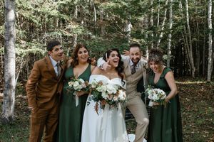 Wedding party poses together in a wooded forest setting with autumn trees and natural lighting.