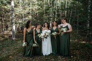 Wedding party poses in forest setting wearing emerald green dresses and white gown for outdoor celebration.
