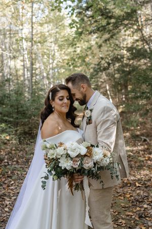 A romantic outdoor autumn wedding scene with a couple embracing among fallen leaves and trees in the forest.