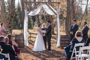 Outdoor wedding ceremony in a wooded setting with white fabric draped between trees and wooden benches for seating.