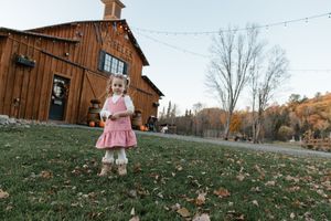 A child plays in autumn leaves scattered across a grassy hill near a rustic wooden barn on a fall afternoon.
