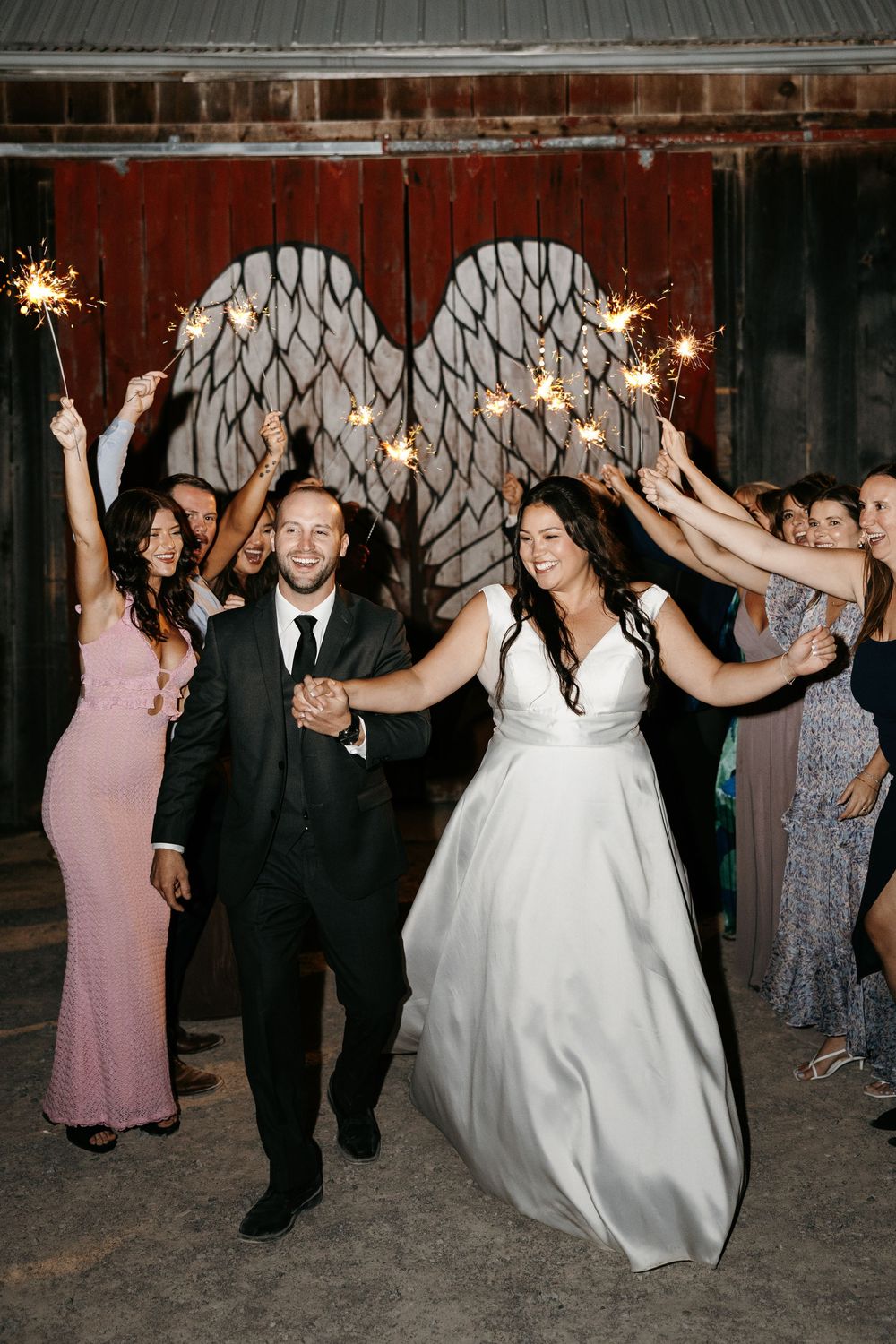 Wedding party guests dance and celebrate together holding sparklers during an evening reception celebration.