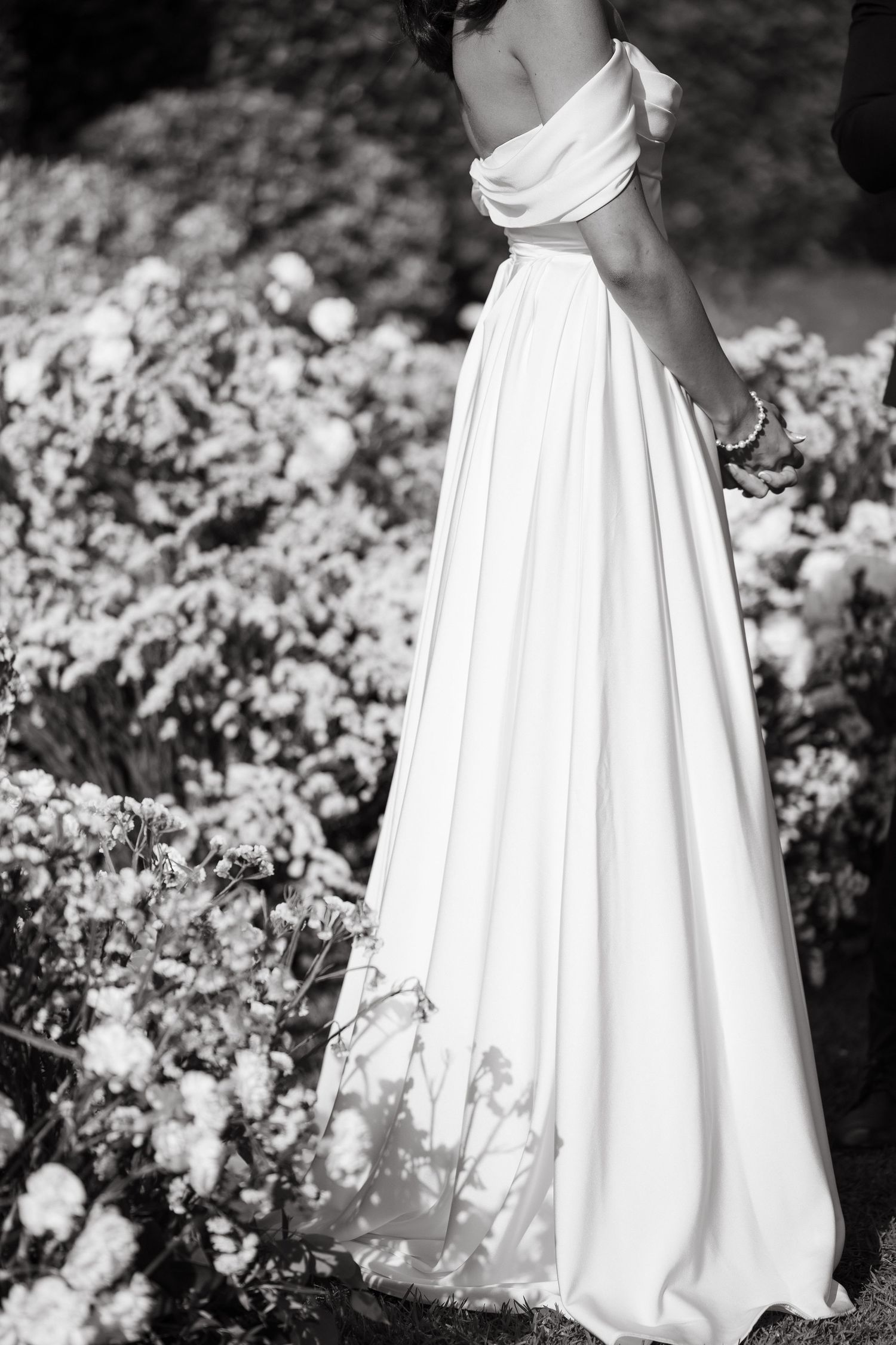 A series of black and white photos showing the bottom half of a white wedding dress among blooming garden flowers.