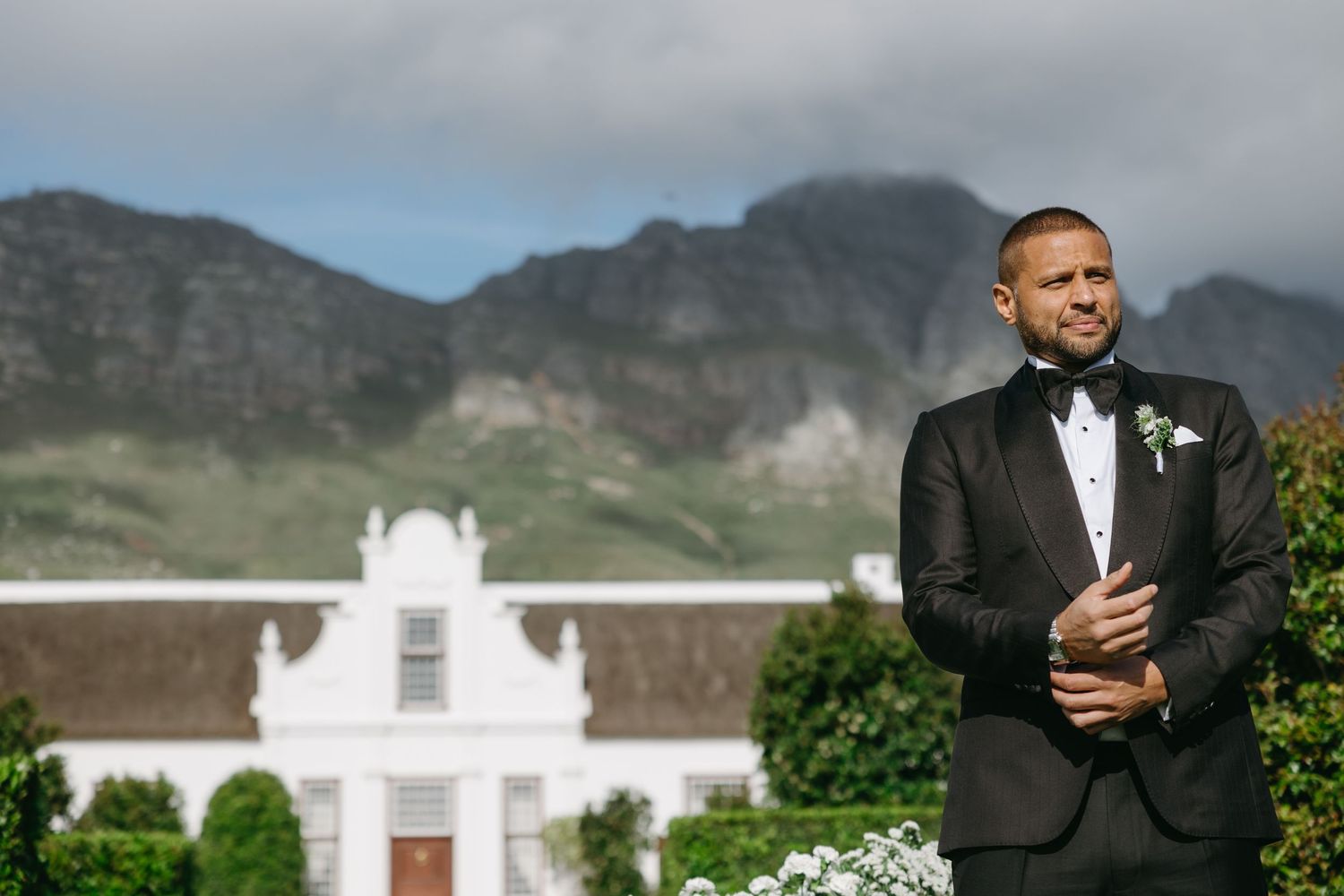 A wedding celebration at a white colonial style venue with mountains and greenery in the background.