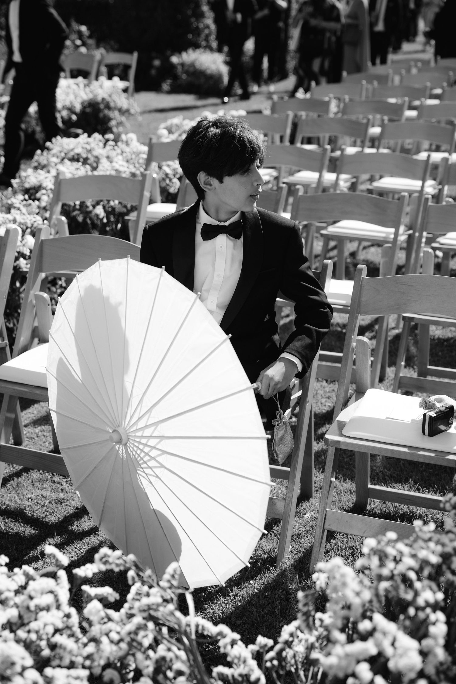 White parasols create an elegant backdrop at an outdoor wedding ceremony among rows of chairs and floral arrangements.