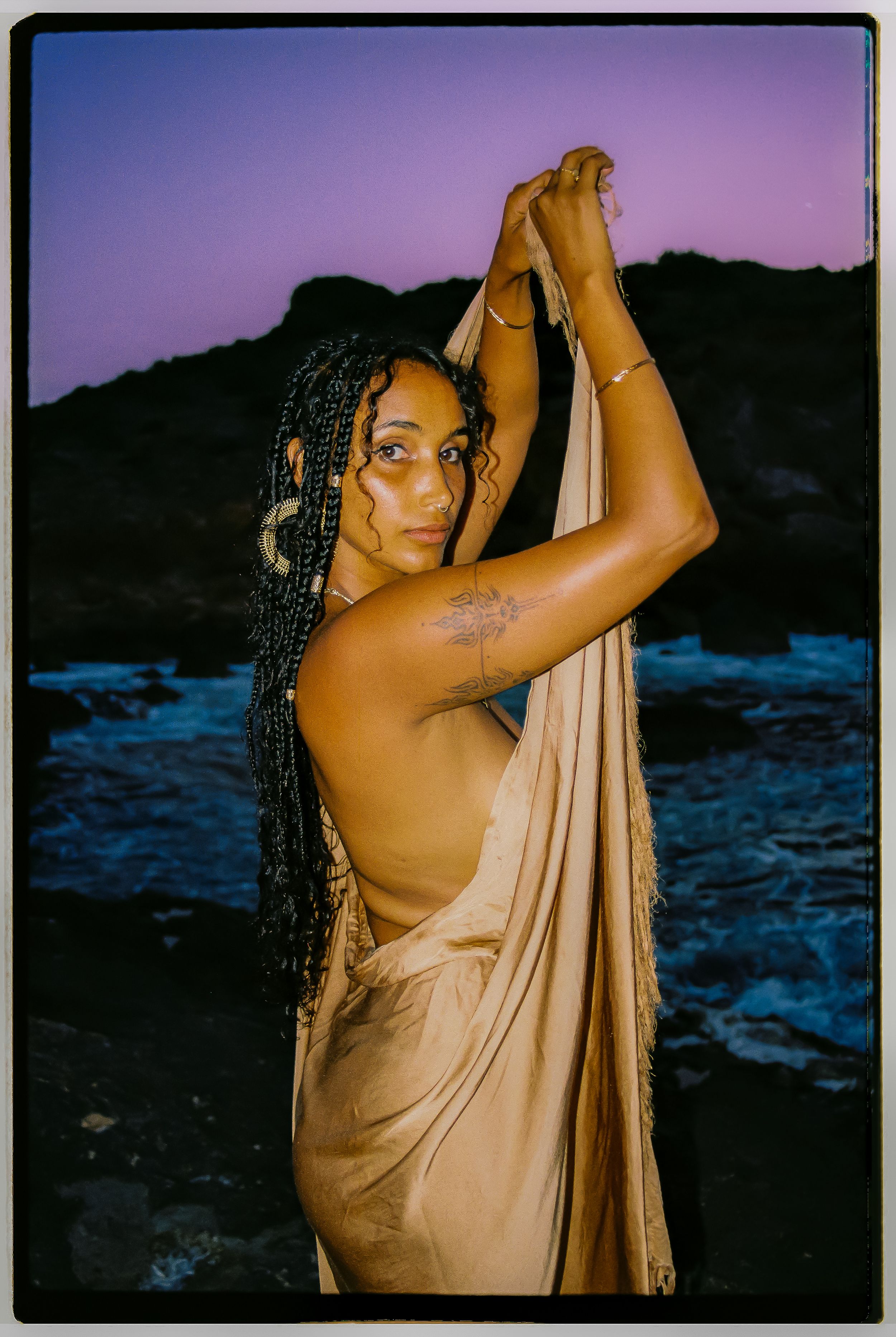 Artistic portrait series of a person wrapped in beige fabric posing against a moody sunset landscape by the ocean.
