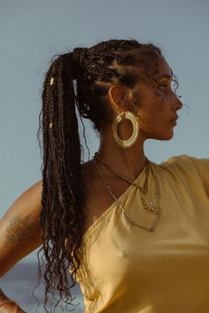 A profile view silhouette against a light background shows long braided hair and gold hoop earrings in warm lighting.