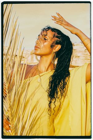 Person with wet curly hair in yellow clothing basking in warm sunlight against a natural outdoor background.
