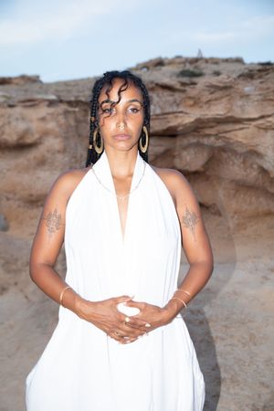 Series of poses in white draped fabric against weathered rock wall.